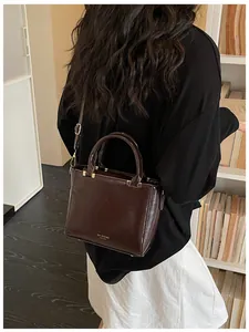 Detail view of dark brown square crossbody bag with adjustable strap worn by model