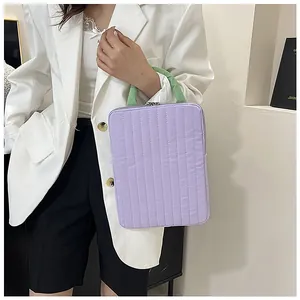 Detail of purple quilted laptop sleeve featuring contrasting green top handles and zipper