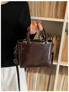 Detail of dark brown glossy patent leather handbag with adjustable strap by a bookshelf