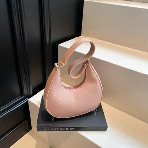 Minimalist light pink crescent hobo bag in pebble leather with gold hardware on a dark base