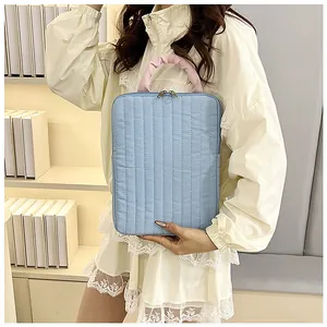 Close-up of light blue quilted laptop sleeve with pink pleated handles in a clean office setting