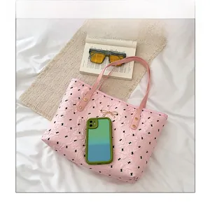 Sac fourre-tout rose avec nœuds noirs, logo doré et objets pour comparaison de taille