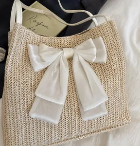 Detail of hand-woven straw bag featuring a large white organza bow and slim strap