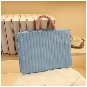 Quilted light blue laptop sleeve with pink ruffled handles and metal zippers on a desk