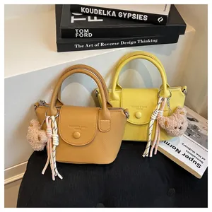 Detail of mini lychee texture PU leather handbags in caramel and yellow with bear charms