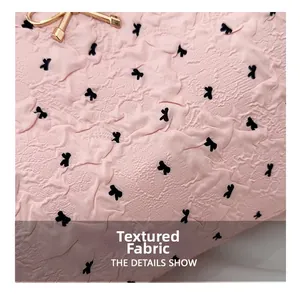 Détail du tissu gaufré rose avec imprimés nœuds noirs et fermoir métallique doré élégant