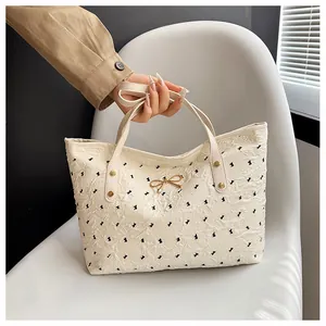 Gros plan d'un sac cabas blanc cassé avec imprimé nœuds noirs et détail en métal doré