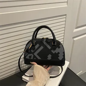 Black shell handbag with grey geometric print and detachable shoulder strap in hand