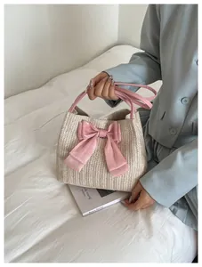 Close-up of straw woven handbag featuring a large pink satin bow and pink faux leather handle