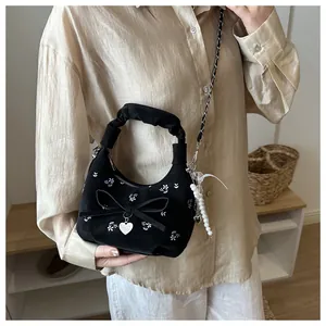 Détail de broderie florale, nœud noir et breloque cœur sur un sac à main plissé