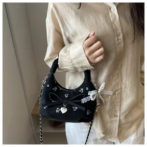 Détail d'un sac à main noir brodé de fleurs avec nœud papillon et pendentif cœur