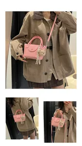 Detail of pink faux leather handbag featuring a teddy bear charm and striped ribbon accent