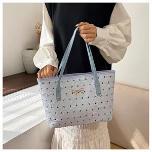 Gros plan du sac cabas bleu clair texturé avec fermoir doré en nœud et motifs noirs