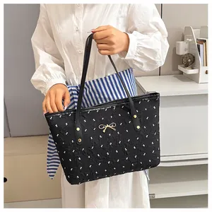 Détail d'un sac cabas noir avec motifs nœuds blancs et accessoire nœud en métal doré
