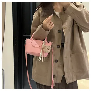 On-body view of a pink textured mini crossbody bag with a plush bear and silk scarf charm