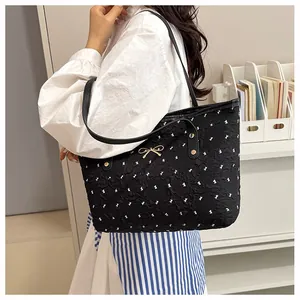Gros plan d'un sac cabas noir matelassé avec motifs nœuds blancs et détail nœud doré