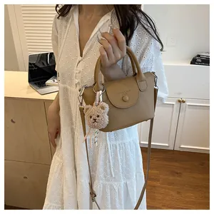 Detail of khaki pebbled leather handbag with detachable strap and teddy bear charm accessory