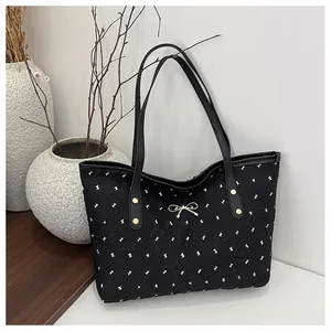 Détail du sac cabas plissé noir avec motifs nœuds blancs et pendentif doré papillon