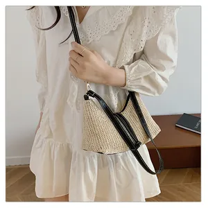 Dettaglio borsa in paglia intrecciata con tracolla in pelle nera e inserti dorati