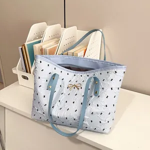 Sac fourre-tout bleu clair à motifs de nœuds avec boucle dorée posé sur un bureau