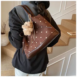 Detailed texture of brown polka dot suede tote bag with smooth leather trim and bear charm