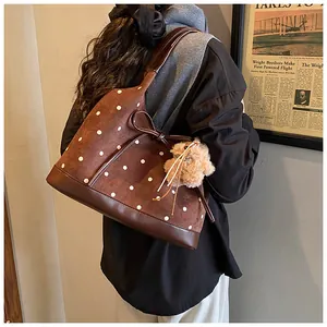 Detailed close-up of brown polka dot suede tote bag with plush bear charm and bow detail