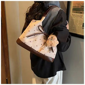 Polka dot canvas tote bag with leather bow and plush bear charm shown on shoulder