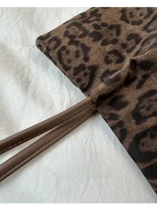 Détail de la bandoulière en cuir synthétique brun sur un cabas en daim léopard
