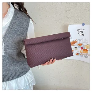 Détail de pochette enveloppe bordeaux avec texture tressée et fermoirs à anneaux argentés