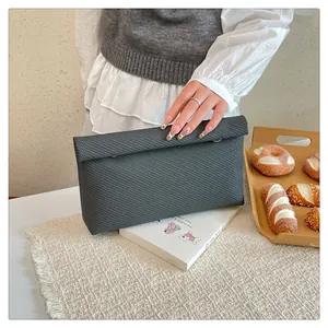 Détail de la pochette enveloppe grise à texture tissée tenue dans un décor lifestyle