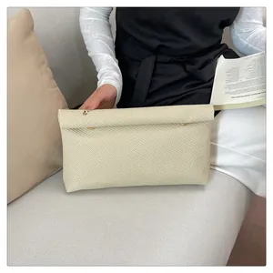 Détail d'une pochette enveloppe tissée beige avec boutons-pression dorés sur un canapé