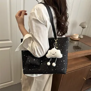 Black tote bag with white star print and plush cloud charm worn by a model
