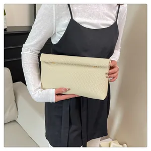 Détail d'une pochette tressée crème avec ornements dorés tenue dans un décor épuré