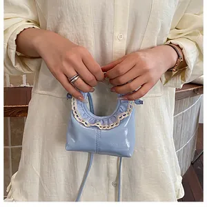Detail of a mini light blue lacquer handbag with white lace trim held by a model