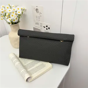 Pochette enveloppe noire texturée avec anneaux dorés sur un bureau blanc minimaliste