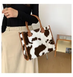 Dettaglio della borsa tote in peluche con stampa mucca e manici in pelle marrone morbida