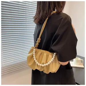 Dettaglio borsa a nuvola beige plissettata con catena di perle e tracolla con nodo su modella