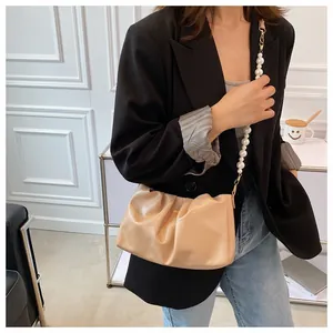 Dettaglio ravvicinato della borsa beige arricciata con elegante catena di perle bianche