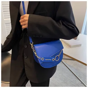 Dettaglio borsa a tracolla blu acceso con catena dorata e logo su un blazer nero