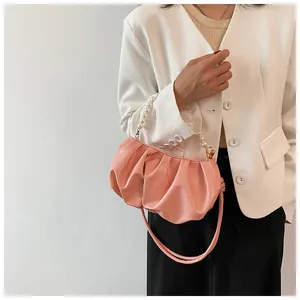 Vista dettagliata di una borsa a nuvola rosa pieghettata con manico di perle e tracolla