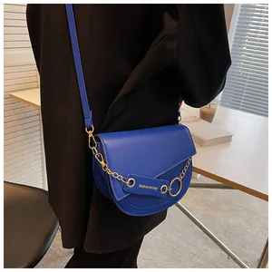 Dettaglio borsa a sella blu con catena dorata ed etichetta in pelle indossata dalla modella
