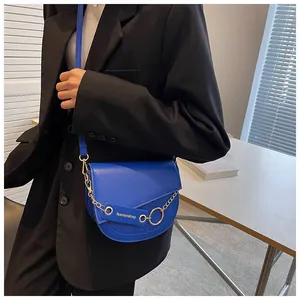 Dettaglio borsa a sella blu con catena dorata e ciondolo indossata da una modella