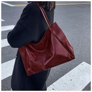 Gros plan d'un grand sac fourre-tout rouge foncé brillant porté à l'épaule en ville