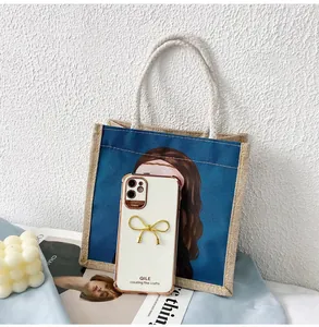 Custodia iPhone bianca con bordo dorato e fiocco, appoggiata su borsa in tela