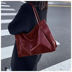 Détail du grand sac cabas bordeaux en cuir brillant porté dans une rue urbaine