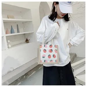 Detail of canvas tote bag featuring red strawberry patterns and woven handles