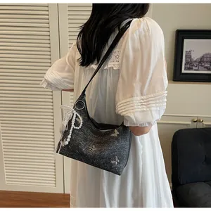 Detail of grey hobo bag featuring silver butterfly studs, lace, and a large pearl charm