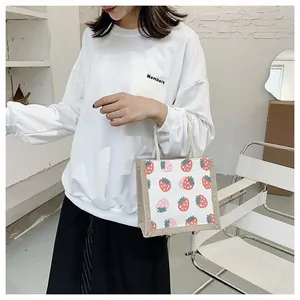Detail of printed linen handbag with strawberry pattern held by model in casual outfit