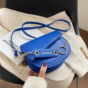 Elegante borsa a sella in pelle blu reale con catena dorata e tracolla su blazer