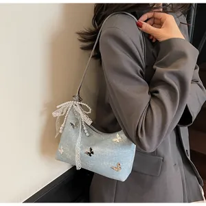 Close-up of light blue shoulder bag with butterfly embroidery and pearl bow charm